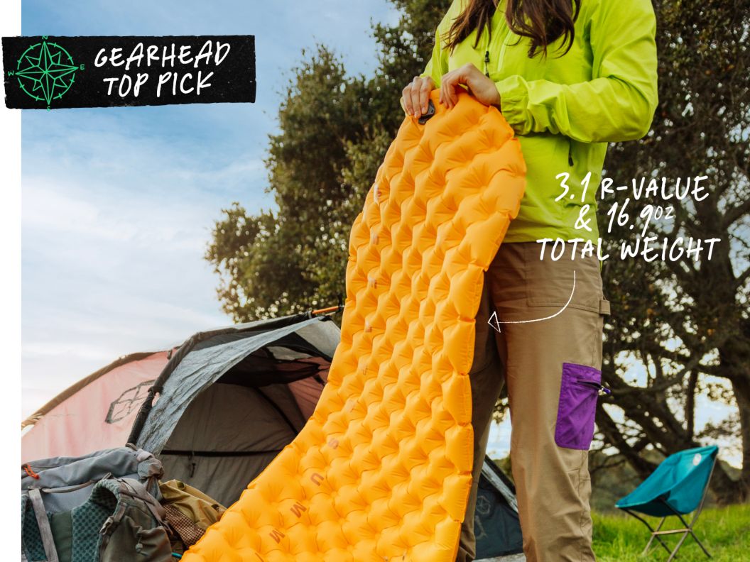 Someone has blown up an orange sleeping pad and they are preparing to put it in a tent. Text overlay reads: Gearhead Top Pick, 3.1 r-value & 16.9oz total weight.
